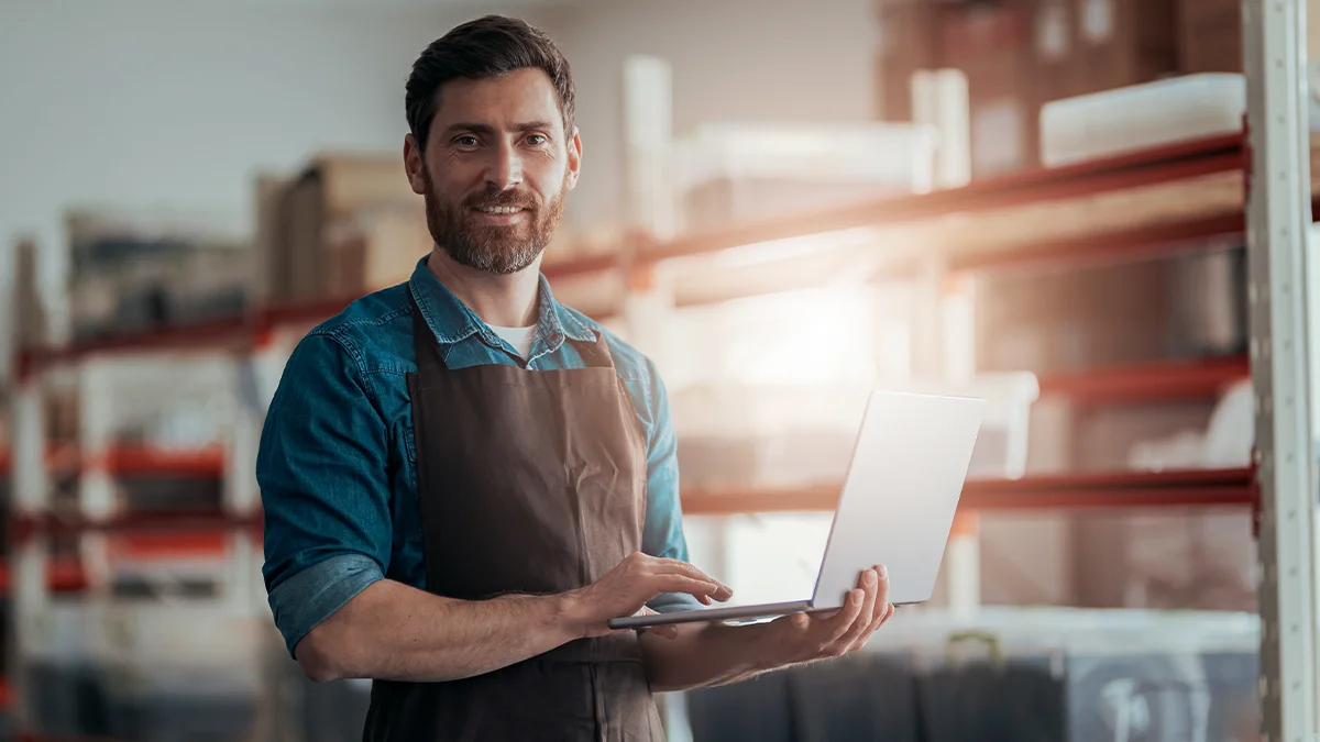Male business owner in warehouse holding laptop